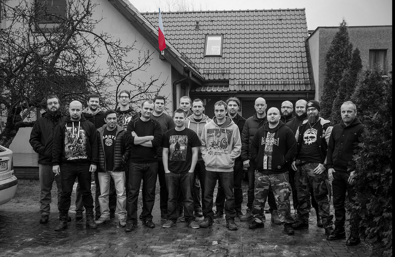 Gruppenfoto des Teams von Destructive Creations in Gliwice vor dem Firmensitz im Jahr 2016. Man sieht insgesamt 18 Männer vor einem Haus stehen, wobei das Foto bis auf eine vermutlich polnische Nationalflagge (rot-weiß) am Dach des Hauses komplett schwarz-weiß ist.